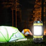 Lampe Camping LED Etanche et Rechargeable via USB la nuit sur fond d'arbres et toiles de tente