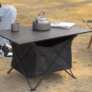 Table de Camping Pliante Ultra Légère avec Sac de Rangement sur fond beige avec une théière et un livre