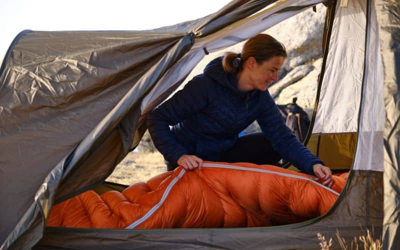 Femme dans une tente ouverte, qui installe son sac de couchage orange.